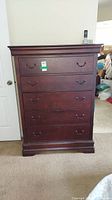 Front view of the tall dresser showing five drawers, metal handles, keyhole on top drawer, and overall condition with light scratches.