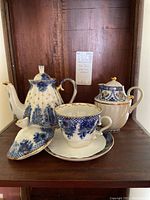 Full view of the teapot, creamer, and cup with saucer showing the blue floral patterns and gold accented trims.