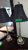 Pair of black hard plastic lamps with black fabric shades, decorative ruffled trim and clear round finials. Lamps have cords wrapped at the base.