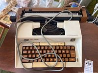 Close-up photo of vintage Coronamatic typewriter showing brown keys with white characters and white/beige body with attached cable.