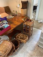Full view of glass cake plate with dome cover, large glass hurricane candle holder, wicker baskets of various sizes, and three-tier wicker shelf unit near wooden table.