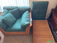 Wicker armchair with green cushions next to matching wicker ottoman with green cushion on top.
