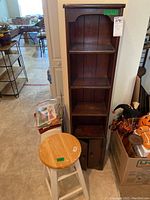 Full view of wood cabinet with open shelves and double-door bottom storage along with wooden stool with round seat.