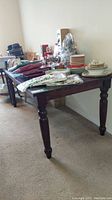 Side angle view of old dark wood dining table with various dishes and cloths on top highlighting the corners and turned legs.