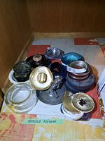 Overview of multiple ashtrays grouped together showing variety in material and size.