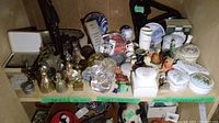 Shelf view showing brass bells, art glass paperweights, porcelain trinket boxes, Delft ball, figurines and metal sculpture