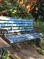 Side view of bench showing peeling blue paint on wooden slats and ornate iron frame.