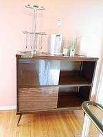 Front view of mid-century wood cabinet showing sliding glass doors on top and wood sliding doors on bottom with items on top surface.