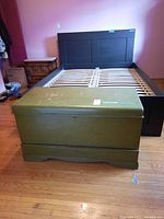 Closed green wooden chest with visible scratches and paint wear in a bedroom setting.