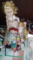 Overall view of the lot showing large blond doll, Raggedy Ann doll, small dolls, and teddy bear on display surface