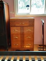 Front view of the tall wooden dresser with 4 drawers and ornate gold-colored handles.
