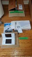 Full view of Nintendo DS Lite console, original box, manuals, and power adapter on cardboard.