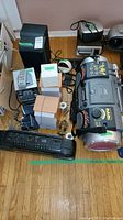 Sony stereo system with speakers, JVC boombox, Sanyo cassette player, Sony alarm clock, remote and other electronics on wood floor.