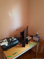 Wide view showing HP Envy printer, monitor, speakers, and cables on a wooden table