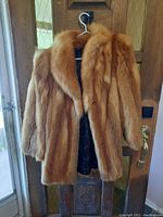 Full view of fox fur lady jacket hanging, showing rich reddish-brown fur and black lining.