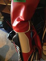 Red and white Sun Mountain golf bag with padded top travel cover, standing upright.