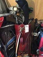 Front and side view of red leather golf bag filled with multiple golf clubs, showing Burton badge and club heads.