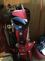 Full view of Adidas red golf bag with head covers for clubs and multiple compartments, with golf clubs inside.