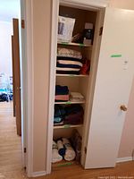 Full view of linen closet with multiple shelves holding folded towels, linens, window panels and bedding items.