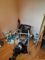 Overview of various medical aids including two walkers, foot massager, inflatable ring, and other mobility accessories on floor by wall.