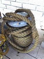 Side view showing the twisted manila rope coiled on the metal spool and a bottle of outdoor lamp oil for size reference.