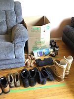 Wide shot showing men's boots and shoes lined up, ladies boots, shoe trees, shoe polishing supplies, shoe horns, and a U-Haul box.