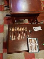 Overhead view of eight ornate teaspoons, three small spoons and one fork on a wooden surface