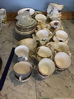 Wide shot showing multiple teacups and saucers on a marble surface, some wrapped in tissue paper.