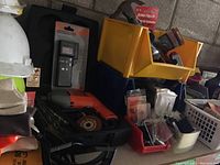 Image shows Black and Decker drill, drill bits, Remington battery tester in packaging, yellow and red plastic bins containing screws and hardware items, and some bottles of oil.