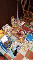View of toys, books, collectible figures, toy cars, dolls, and chairs on floor in basement corner.