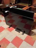 Front view of the Insignia flat-screen TV with remote control placed in front on the floor.