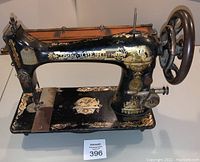 Side view of black cast iron Singer sewing machine head showing gold and white Egyptian Sphinx and winged graphics, and functional hand wheel and lever.