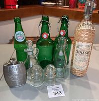Photo showing all items together on a table, including wicker-covered Triple Sec bottle, green glass bottles, Hemingray insulators, and Jack Daniel's flask.
