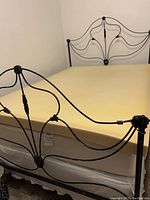Photo of a yellow memory foam mattress topper, about 3 inches thick, fitting on a double metal bed frame with a decorative headboard and footboard.