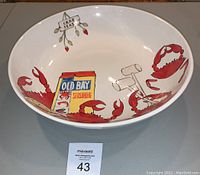 Photo showing the bowl interior with red crab claws, Old Bay seasoning box illustration, and crab feast sign.