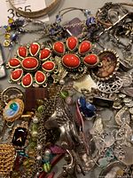 Top view of assorted vintage costume jewelry with red teardrop floral brooches, chains, and mixed pieces, showing condition and variety.
