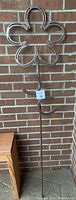 Full view of large horseshoe flower yard art stake against brick wall, showing entire height and shape.