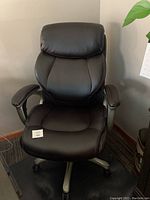 Front view of black leather ergonomic office chair showing cushioned seat, headrest, and armrests with rolling casters below.