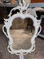 Full view of the ornate white French country chic wall mirror with carved floral and scroll details, showing the overall design and shape.