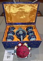 Miniature blue and white dragon motif teaset with six cups, teapot in a blue satin brocade box with golden interior, red octagonal sewing trinket box in front.