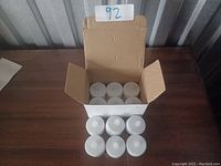 Box opened displaying 12 white electric tea-light candles arranged inside the packaging with a 92 lot number marker.