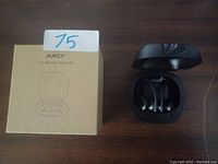 Photo showing Aukey True Wireless Earbuds in black inside their charging case, alongside the original cardboard box packaging with the Aukey logo and model name.