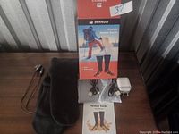Black Bernuly electric heated socks laid out on table with original packaging box, dual batteries, charging adapter, and user manual.