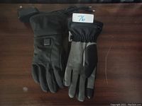 Pair of black and gray heated gloves placed side by side, showing front and back views, with a control button visible on one glove and power cables connected.
