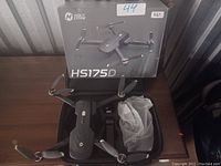 HolyStone HS175D drone, remote controller, propeller guards, USB charging cable, carrying case, and original box displayed on a table.
