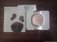 Photo showing pink HTC wireless earbuds charging case in packaging next to original box.