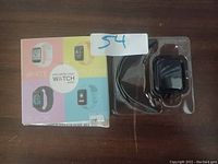 Photo of Macaron Color Smart Watch in black sealed packaging, with original box showing multiple color options, and a charger cable.