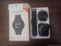 Photo showing smart bracelet in box with strap, charger cable, and charging dock