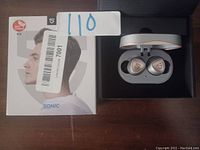 Soundpeats Sonic earbuds in charging case next to original retail box on wooden surface.
