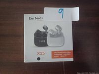 Photo of the X15 True Wireless Earbuds retail packaging showing black and white color options and charging case with LED display.